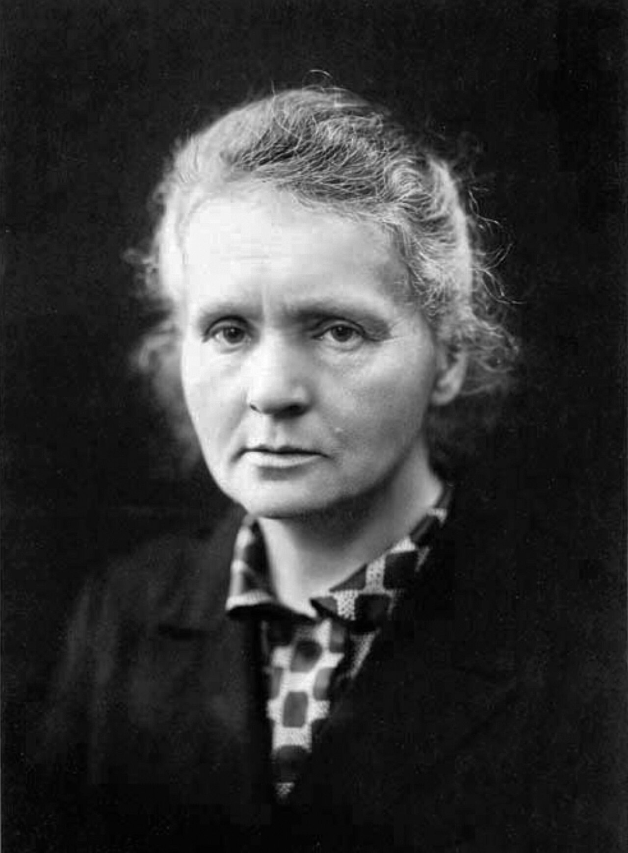 Marie Curie in a dark high-collared dress, seated at her laboratory desk.